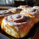 Close-up of freshly baked Cinnabon rolls covered in sweet, creamy icing on a tray.