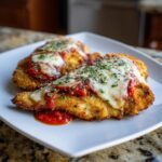 Two pieces of golden Air Fryer Chicken Parmesan topped with tomato sauce, melted mozzarella, and herbs on a white plate.