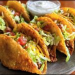 Close-up of Air Fryer Tacos Extravaganza filled with ground beef, lettuce, tomato, and cheese, served with sour cream.