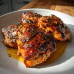 Three pieces of juicy Balsamic Baked Chicken Breast on a white plate, glistening with sauce and herbs.