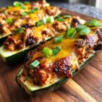 Close-up of BBQ Chicken Zucchini Boats topped with melted cheese and green onions on a wooden board.