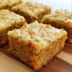 Close-up of Carrot And Zucchini Bars with cream cheese frosting, showing the moist texture and shredded vegetables.