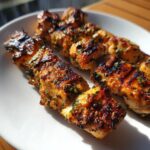 Three grilled Chicken Skewers with Garlic and Parmesan on a white plate, showing grill marks and herb garnish.
