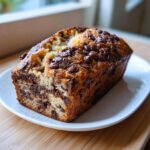 A loaf of Chocolate Espresso Banana Bread with chocolate chips on a white plate.