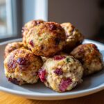 A stack of golden-brown Cranberry Turkey Stuffing Balls on a white plate, flecked with cranberries and herbs.