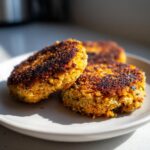 Three Crispy Sweet Potato Lentil Patties stacked on a plate, showcasing their golden-brown crust.