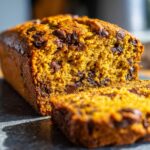Close-up of a loaf of Decadent Pumpkin Bread with Chocolate Chips, with a slice cut.