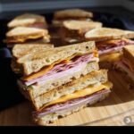 Close-up of stacked DIY Coffin Sandwiches Halloween with ham and cheese filling on a wooden board.