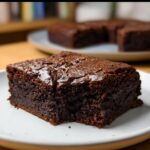 A single slice of flourless greek yogurt brownie on a white plate, with a bite taken out.