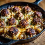 A cast iron skillet filled with French Onion Meatballs, caramelized onions, and melted cheese.