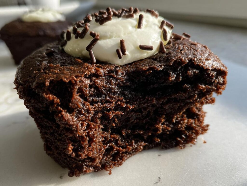 Close-up of a fudgy Protein Brownie with a bite taken out, topped with cream and chocolate sprinkles.