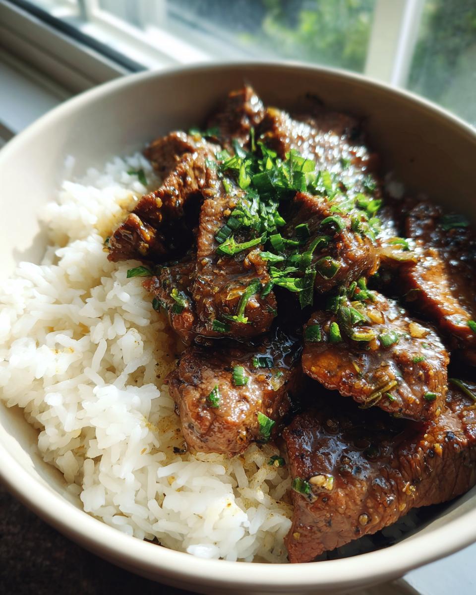 A bowl of Garlic Butter Beef and Rice, garnished with fresh herbs, sits near a window.