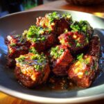 A close-up of Garlic Butter Beef Bites, glistening with sauce and topped with fresh parsley, served on a gray plate.