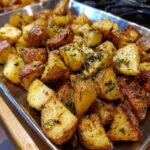 Close-up of Garlic Herb Roasted Potatoes on a metal baking sheet, seasoned with herbs.