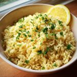 A bowl of Greek Lemon Rice, garnished with fresh parsley and a lemon wedge.