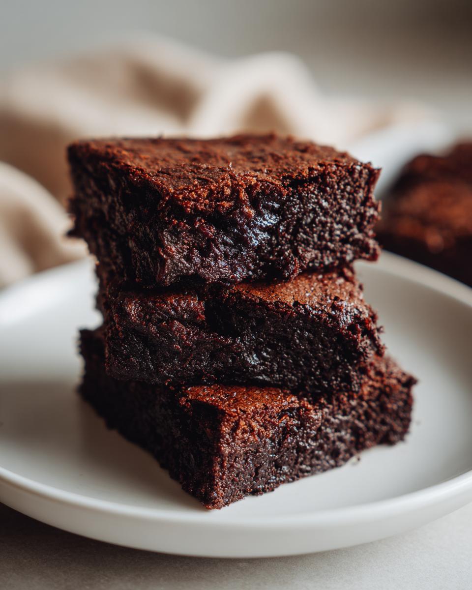 A stack of three Healthy 87 Calorie Brownies on a white plate, showcasing their rich chocolate texture.