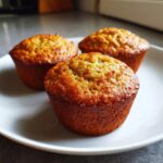 Three healthy banana oatmeal muffins arranged on a white plate, ready to eat.
