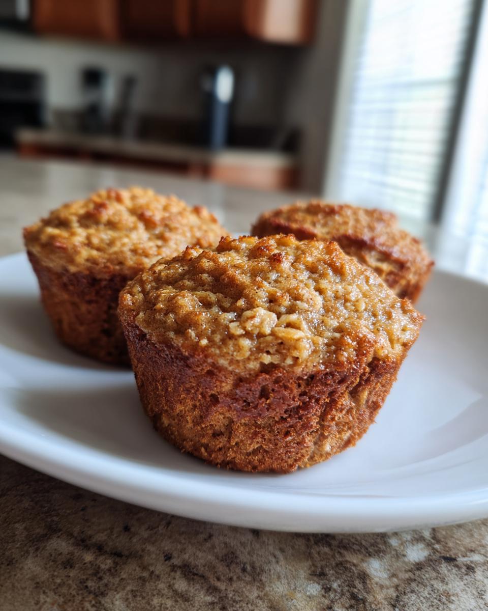 Three healthy banana oatmeal muffins arranged on a white plate, showcasing their texture and golden-brown color.