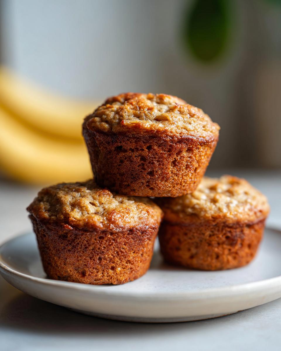A stack of three Healthy Banana Oatmeal Muffins on a white plate, with bananas in the background.