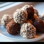 A plate of Healthy Chocolate Chickpea Truffles, some coated in nuts and others in cocoa powder.
