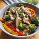 A colorful and appetizing Healthy Steak Bowl featuring sliced steak, quinoa, broccoli, peppers and a creamy sauce.