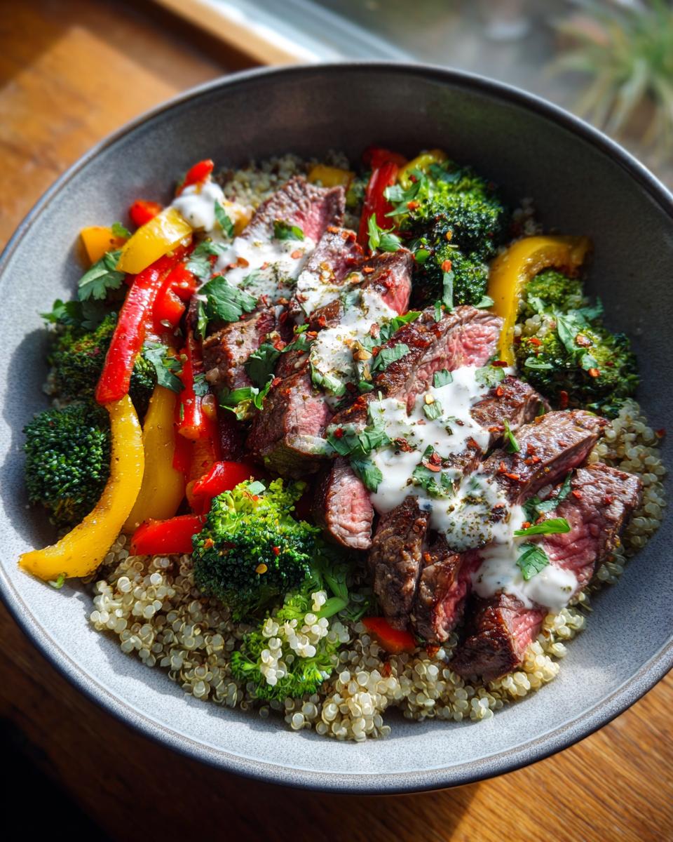 Overhead shot of a Healthy Steak Bowl with sliced steak, quinoa, broccoli, peppers, and a creamy sauce.