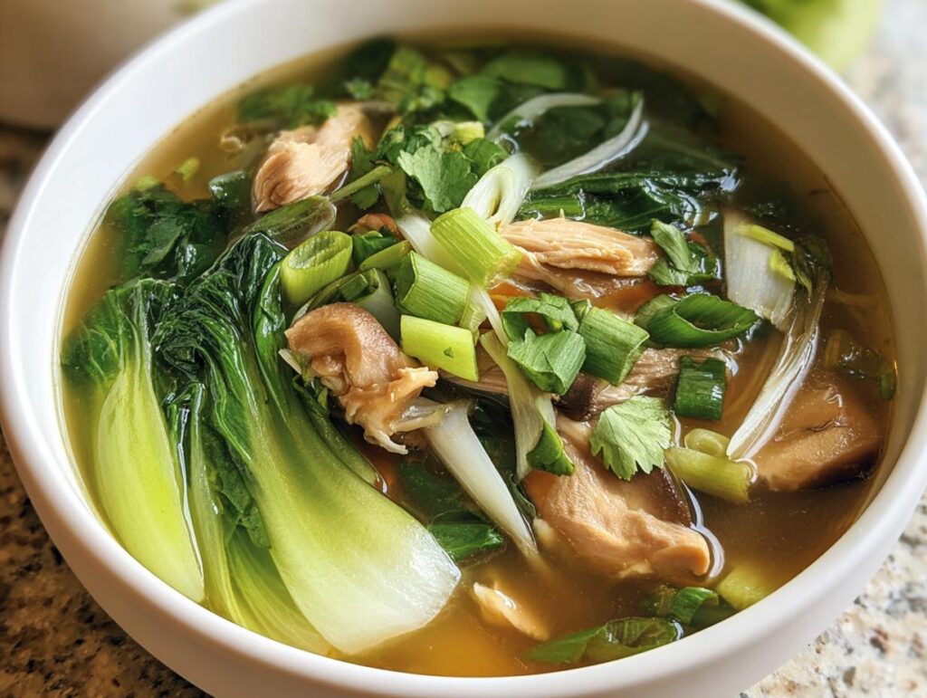 A bowl of Hearty Bokchoy Chicken Soup with bok choy, chicken, mushrooms, and garnished with green onions and cilantro.
