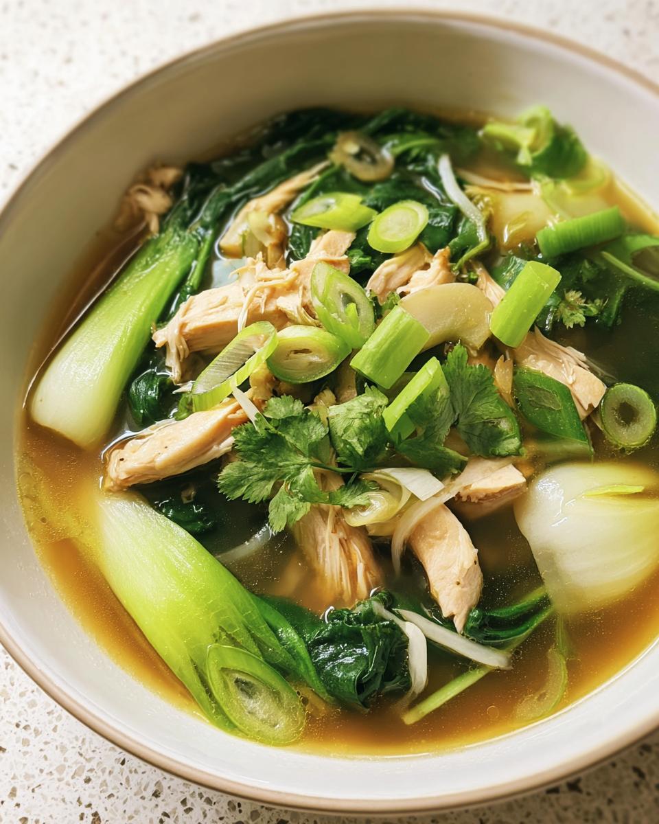 Close-up of a bowl of Hearty Bokchoy Chicken Soup, featuring bok choy, chicken, and green onions in a flavorful broth.