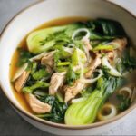 Close-up of a bowl of Hearty Bokchoy Chicken Soup with chicken, bok choy, and garnished with herbs.