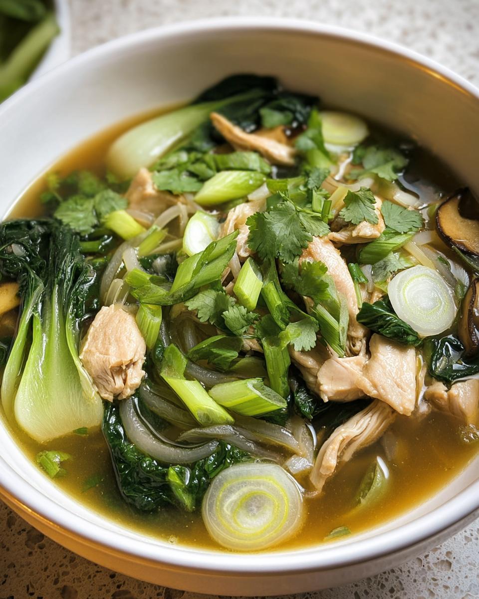 Close-up of a bowl of Hearty Bokchoy Chicken Soup with chicken, bok choy, and garnished with cilantro and green onions.