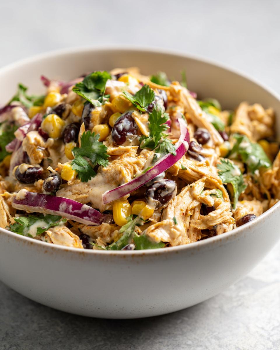 A bowl of High Protein Southwest Chicken Salad with chicken, corn, black beans, red onion, and cilantro.
