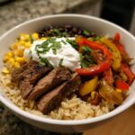 A delicious High Protein Steak Fajita Bowl filled with steak, rice, peppers, corn, black beans, and sour cream.