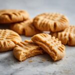 A close-up of Homemade Copycat Nutter Butters, one broken in half to show the peanut butter filling.