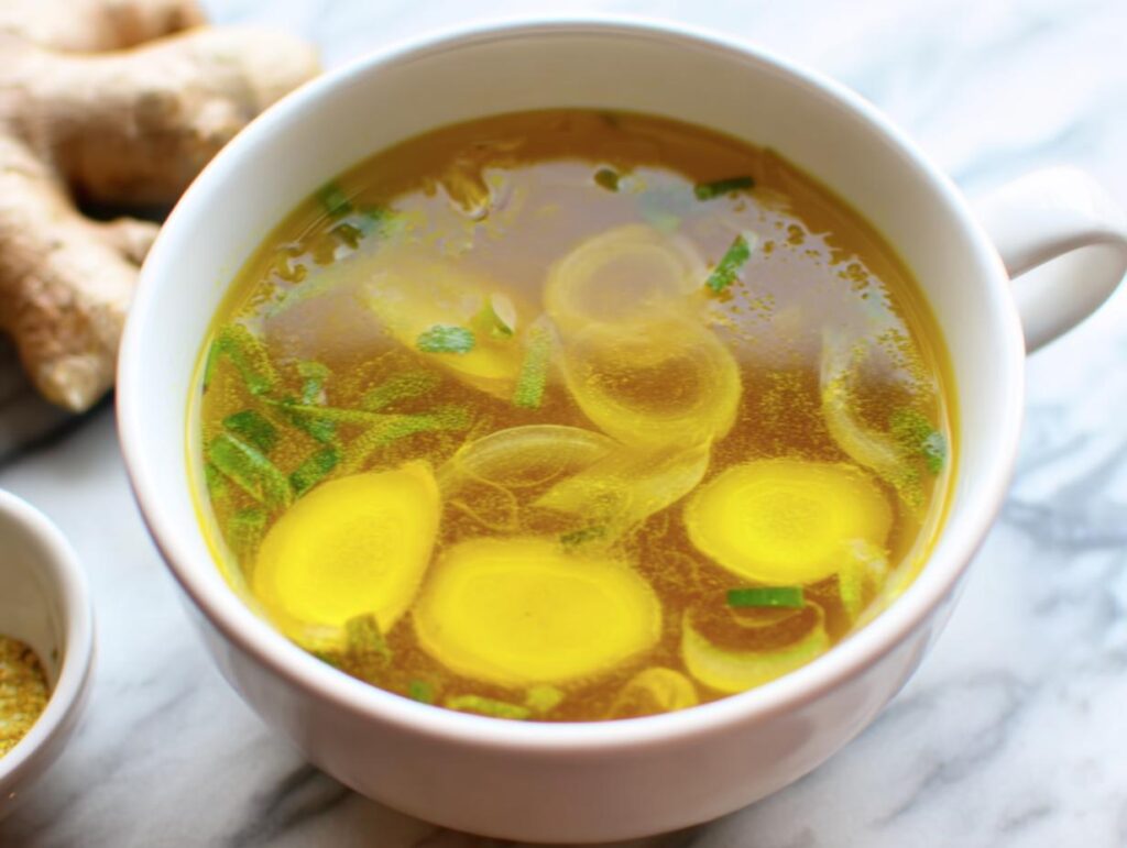 Close-up of Immune Boosting Broth in a white bowl with ginger and spices on a marble surface.