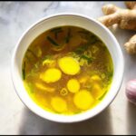 Overhead shot of a bowl of Immune Boosting Broth with ginger slices and green onions.