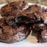 A plate of decadent Keto Flourless Fudge Cookies, one broken in half to show the fudgy center.