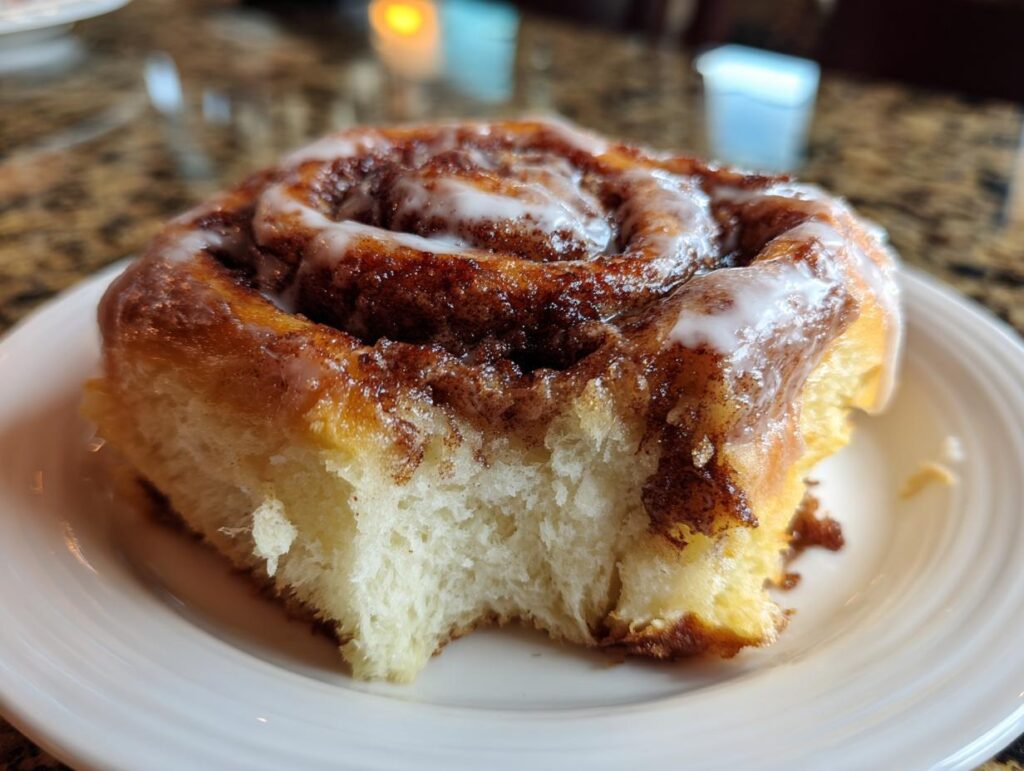 Cinnamon roll with a bite taken out of it, glazed and on a white plate. Keto Garlic Butter Meatballs recipe blog.