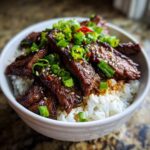 Close-up of a Korean BBQ Steak Rice bowl, topped with green onions and sesame seeds.