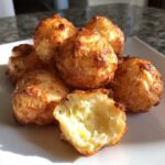 A close-up of golden brown Mashed Potato Puff Bites, one broken open to show the fluffy interior.
