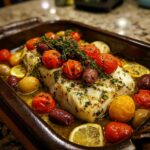 Mediterranean Baked Fish with cherry tomatoes, olives, lemon slices, and herbs in a baking dish.