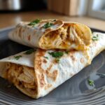 Two melty garlic chicken wraps stacked on a plate, garnished with fresh parsley.