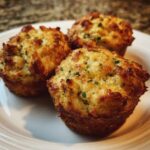 Three golden Parmesan Zucchini Muffins on a white plate, ready to eat.