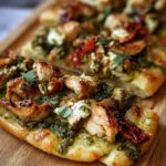 Close-up of Pesto Chicken Flatbread featuring grilled chicken, pesto, tomatoes, and cheese on a wooden board.
