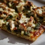 A close-up of a slice of Pesto Chicken Flatbread, topped with pesto, chicken, and parmesan.
