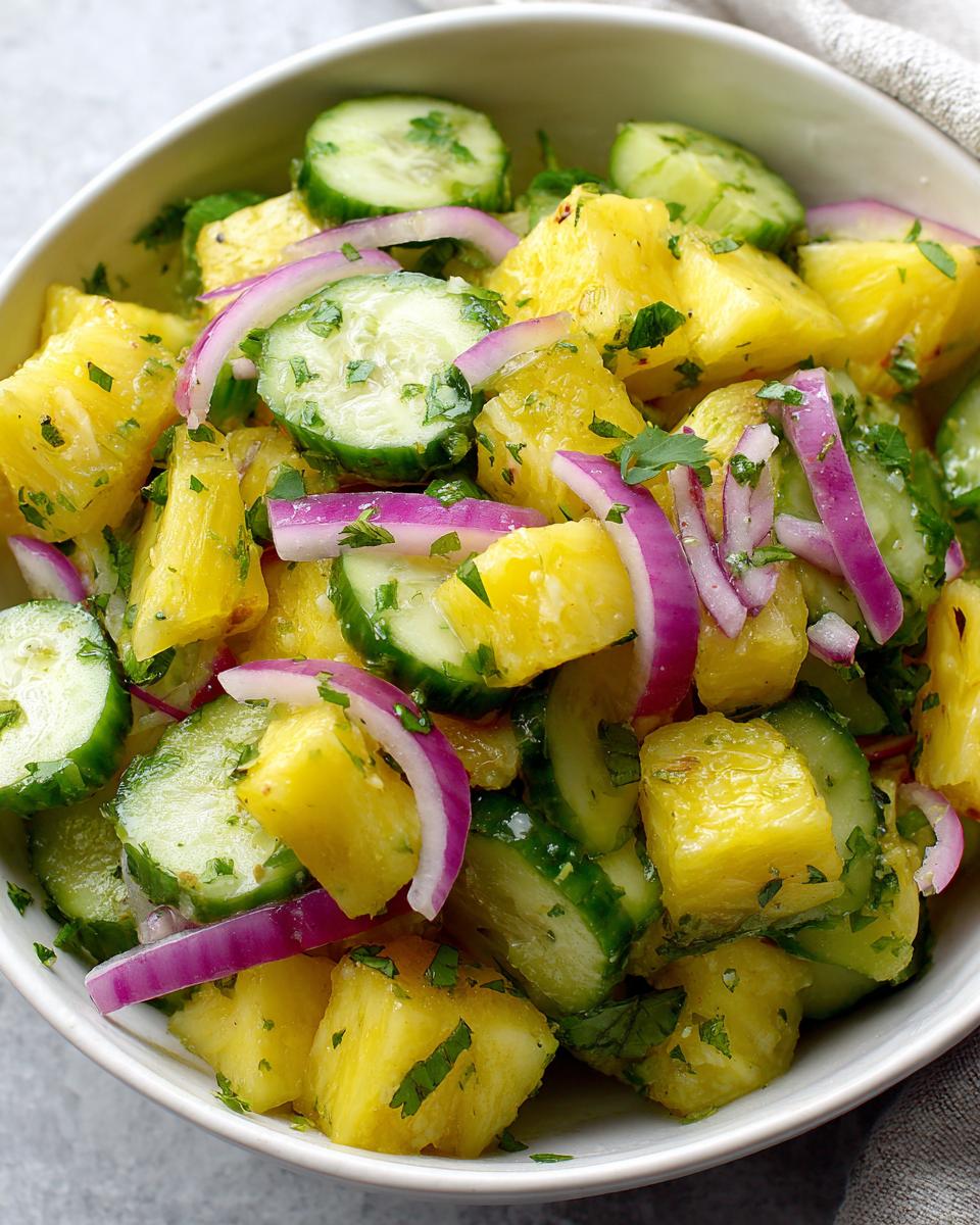 A vibrant bowl of Pineapple Cucumber Salad with red onion and herbs, ready to serve.