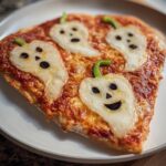 A slice of pizza margherita halloween decorated with ghost-shaped mozzarella and green pepper stems.