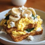 Toast topped with scrambled eggs, spinach, banana, and cheese. A tasty high protein breakfast recipes idea.