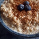 Close-up of Quinoa Pudding in a blue bowl, topped with cinnamon and fresh blueberries.