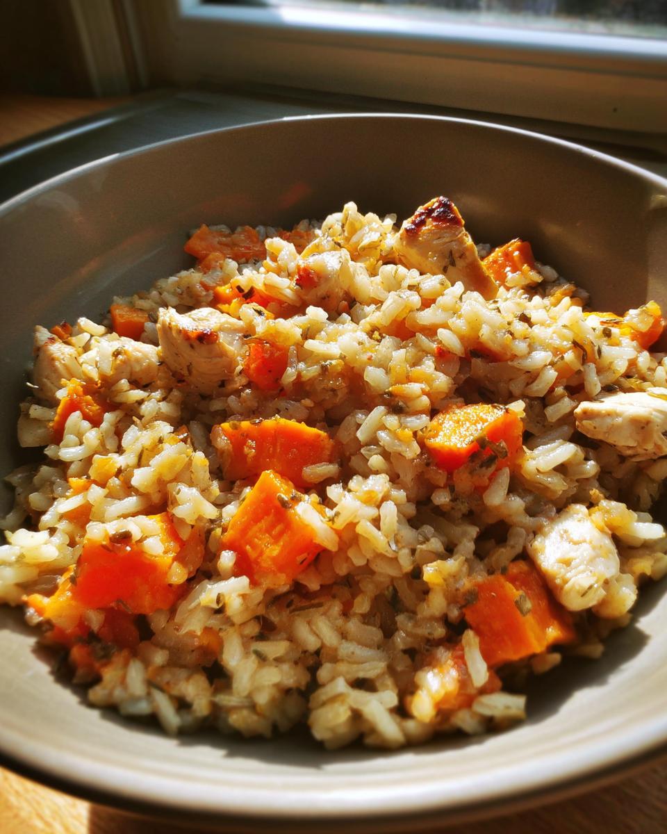 Bowl of rice mixed with diced chicken and orange vegetables, possibly sweet potatoes or carrots.