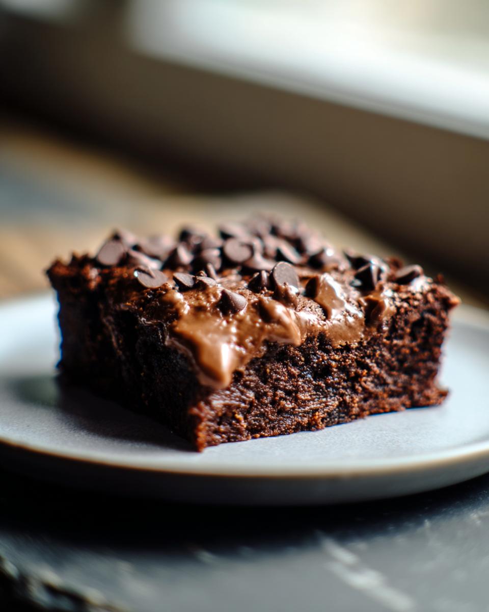 A single slice of Secretly Healthy Zucchini Brownies topped with chocolate chips on a plate.